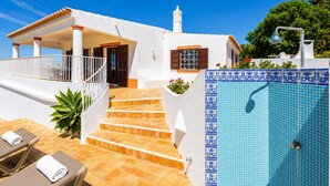 Eine weiße Villa mit Pool, Treppen zu einer überdachten Terrasse und einem Garten.