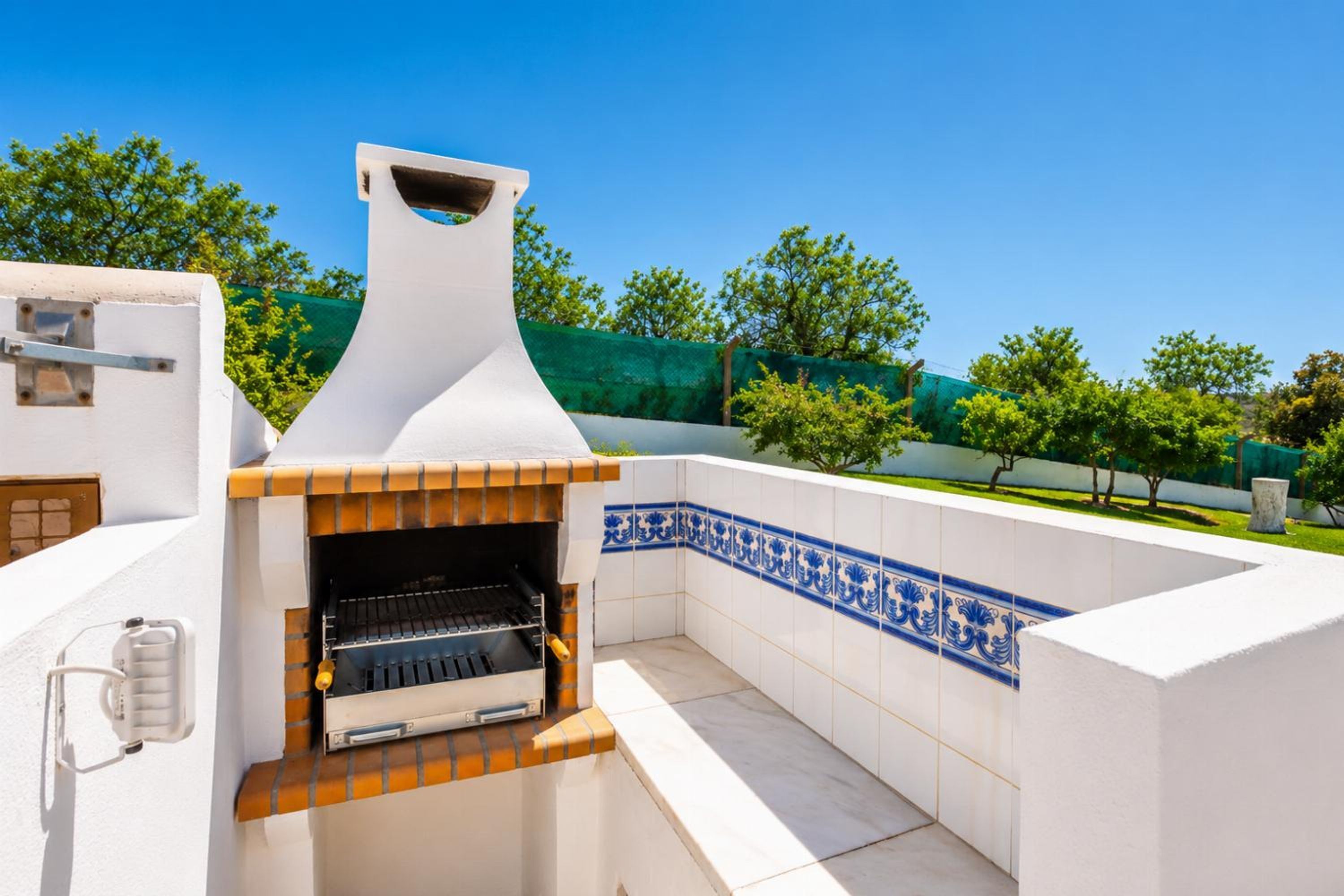 An outdoor kitchen with a grill, surrounded by white walls with blue decorative tiles.