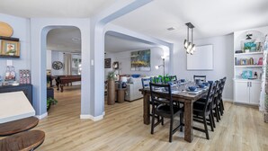 Un comedor con mesa y sillas de madera, una cocina con gabinetes blancos y una sala de estar con un sofá y un cuadro.