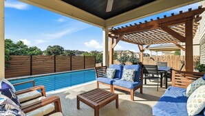 Un patio exterior con piscina, muebles de madera y una pérgola.