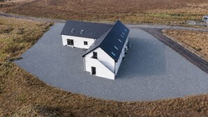 A two-story building with a sloped roof, a gravel driveway, and a fenced area.
