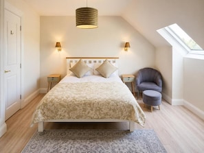A bedroom with a bed, two bedside tables, a chair, a window, and a skylight.