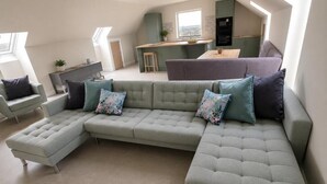 A modern living room with a sectional sofa, a dining area, and a kitchen in the background.