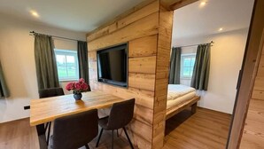 A wooden interior with a bed, a TV mounted on the wall, a dining table with chairs, and curtains on the windows. - Vacation Rental in Salzburg (Salzburg)