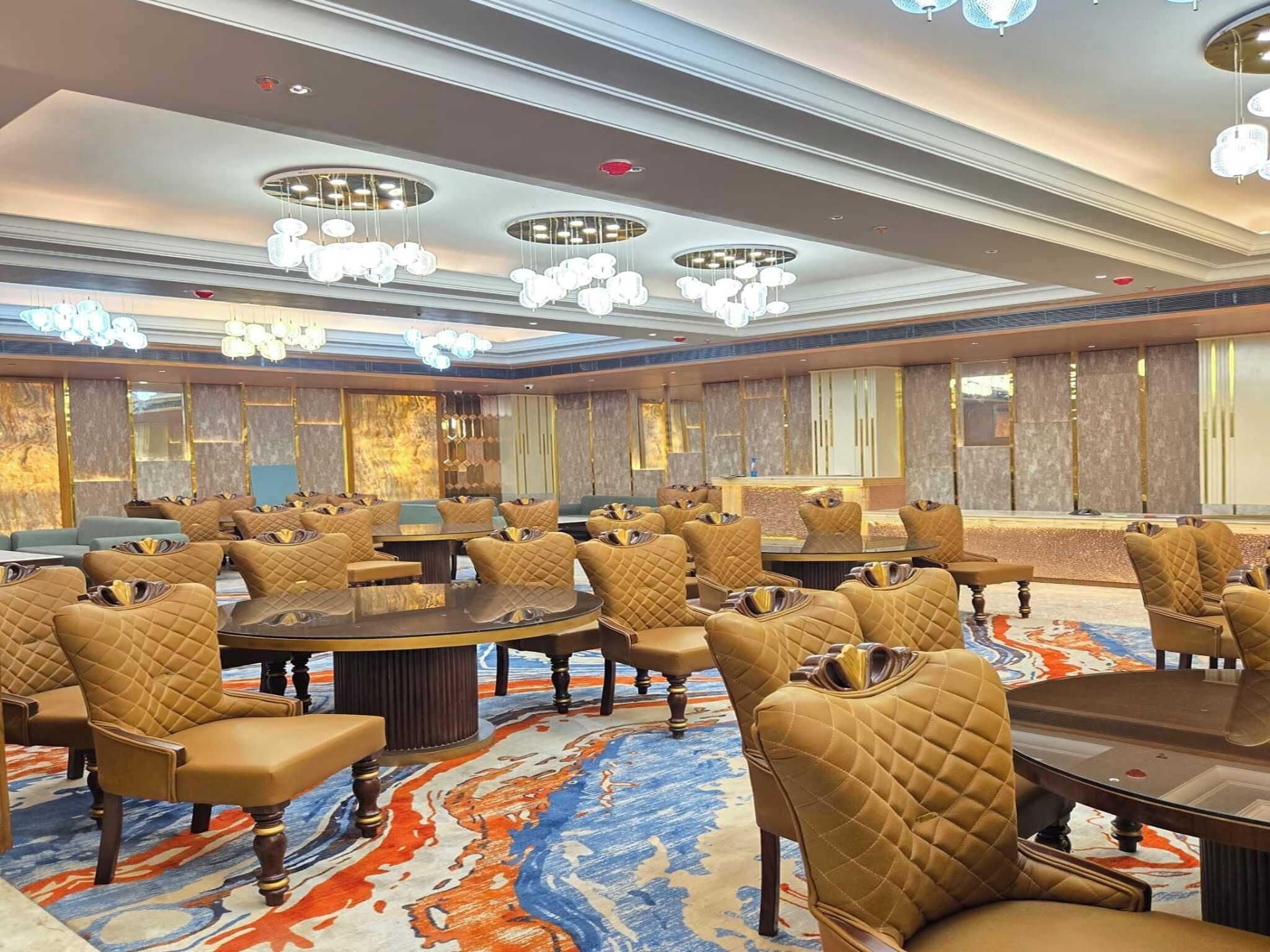 A spacious conference room with round tables and chairs, a patterned carpet, and a modern chandelier.