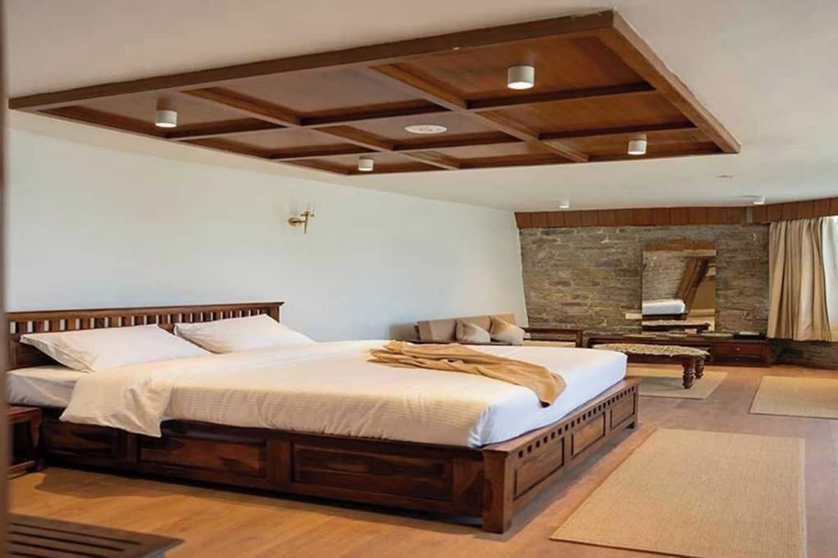 Un dormitorio con una cama grande, vigas de madera en el techo, una pared de piedra y un banco de madera.