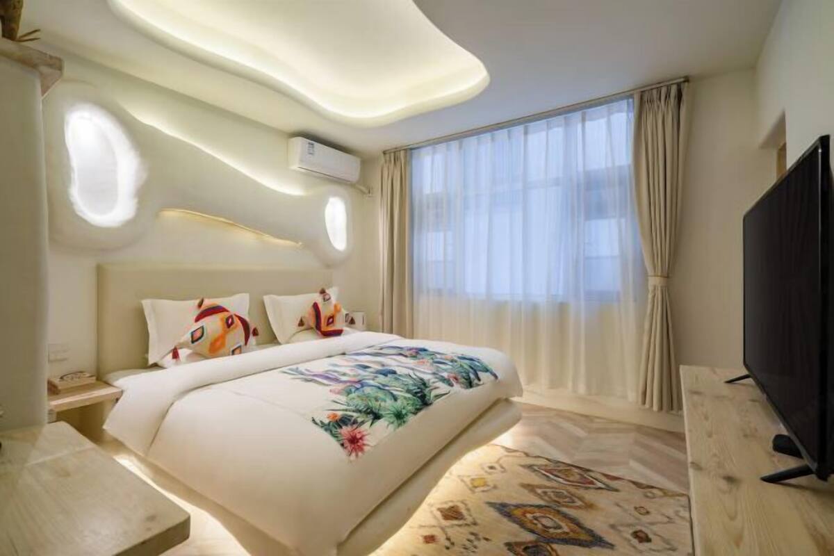 A hotel room with a bed, a TV, a desk, and a window with curtains.