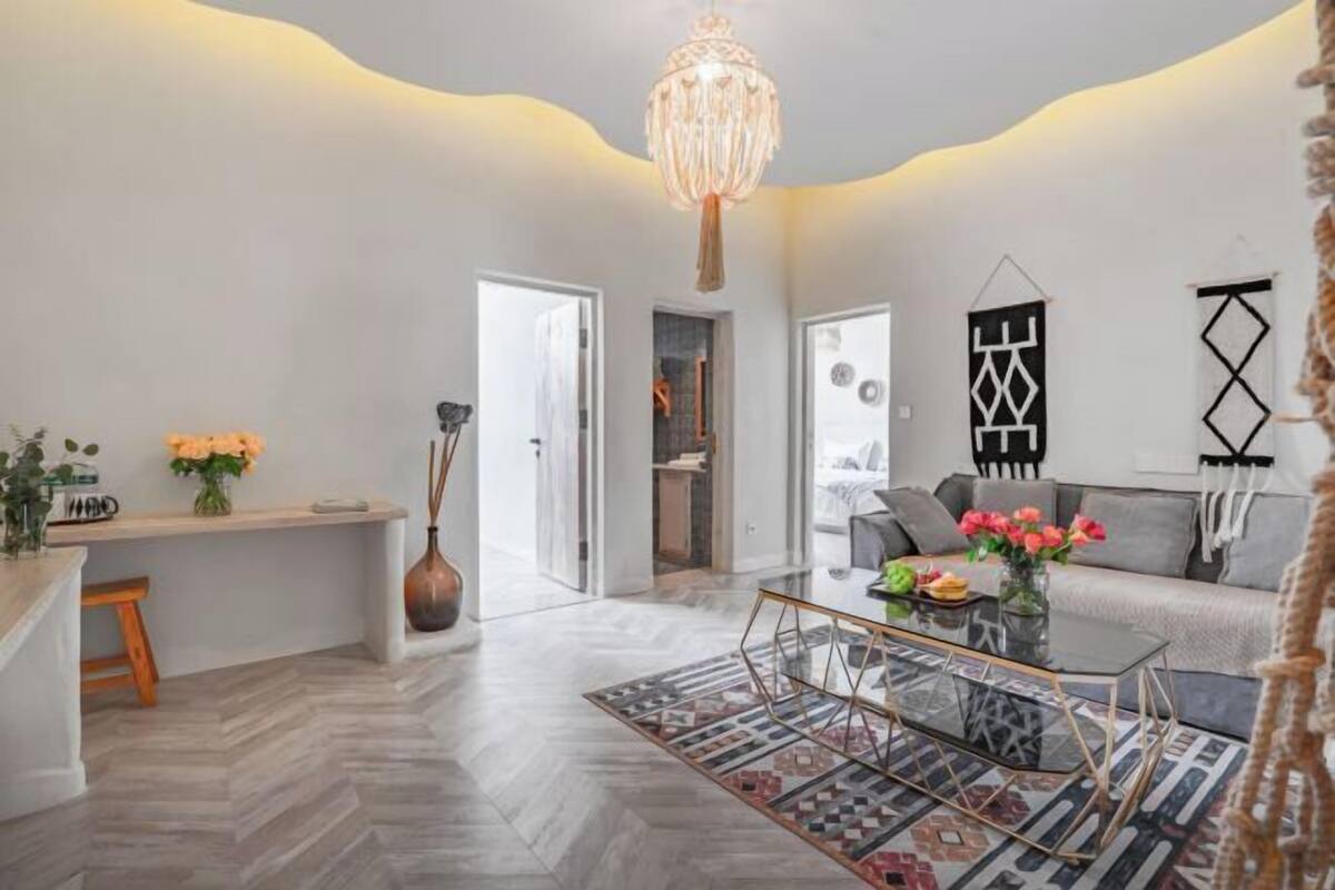 A modern living room with a glass coffee table, a sofa, and a chandelier.