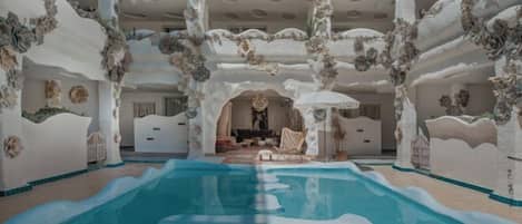Una piscina interior con una zona de estar central, rodeada de paredes blancas con motivos florales.