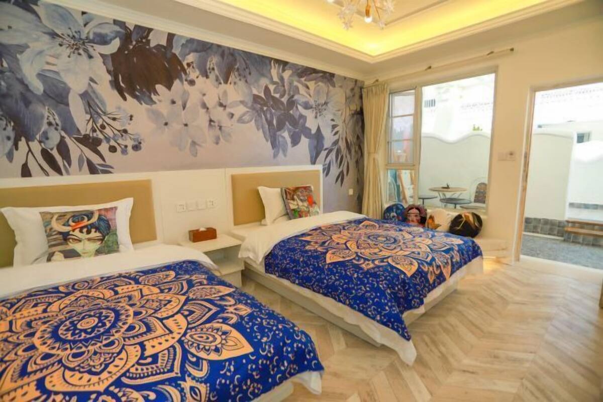 A hotel room with two beds, a large floral mural, and a view of the outside.