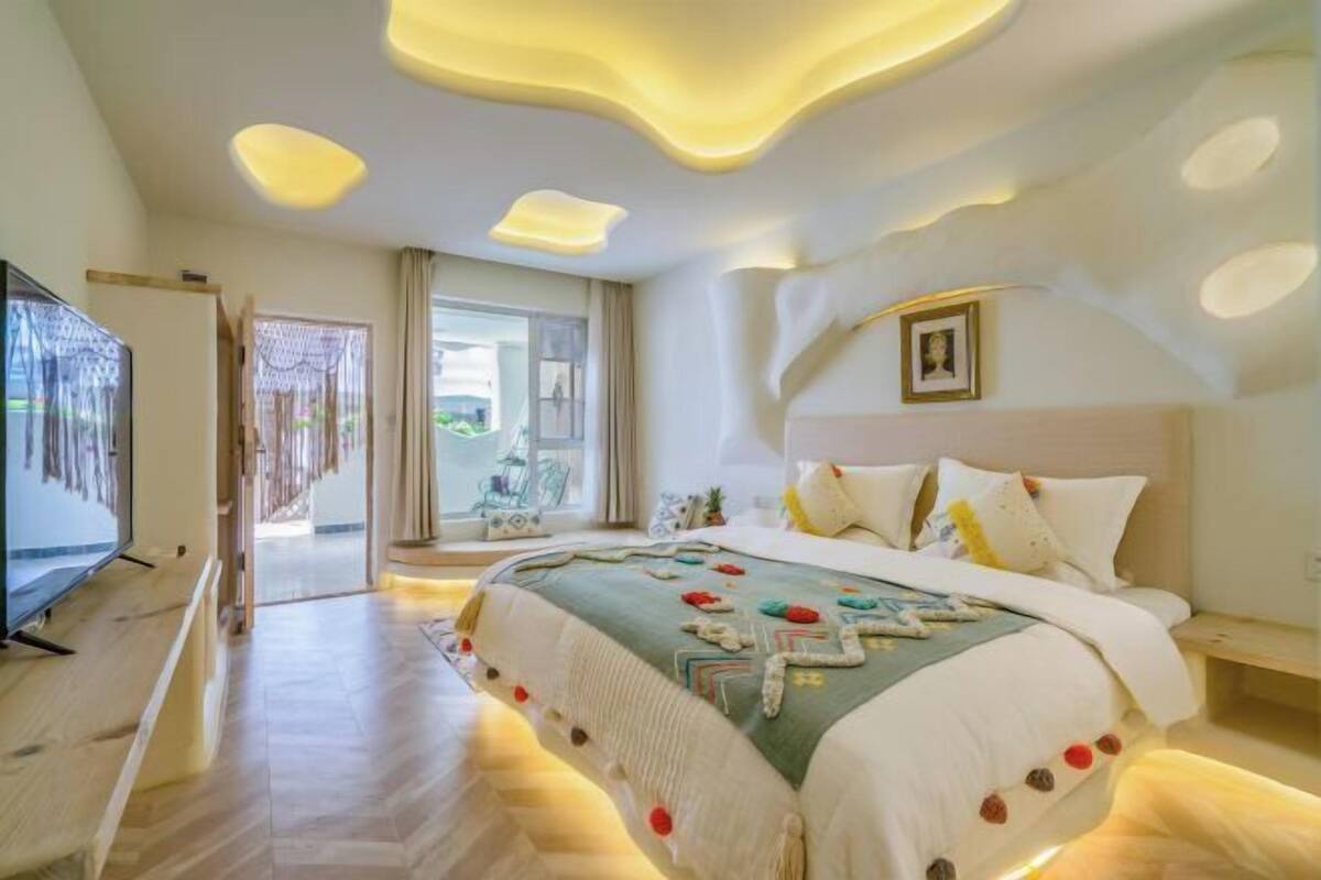 A modern bedroom with a large bed, a television, and a balcony.
