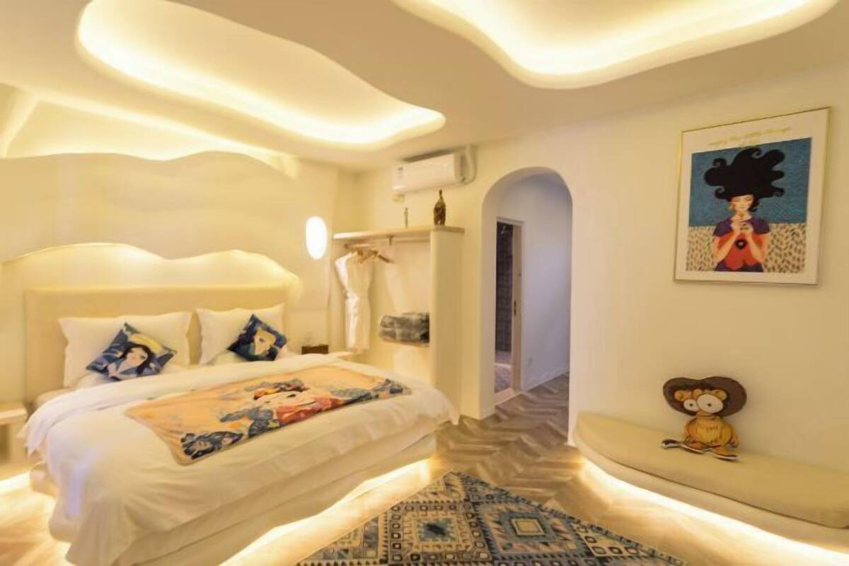 A bedroom with a bed, a bench, a wall-mounted artwork, and a door leading to another room.