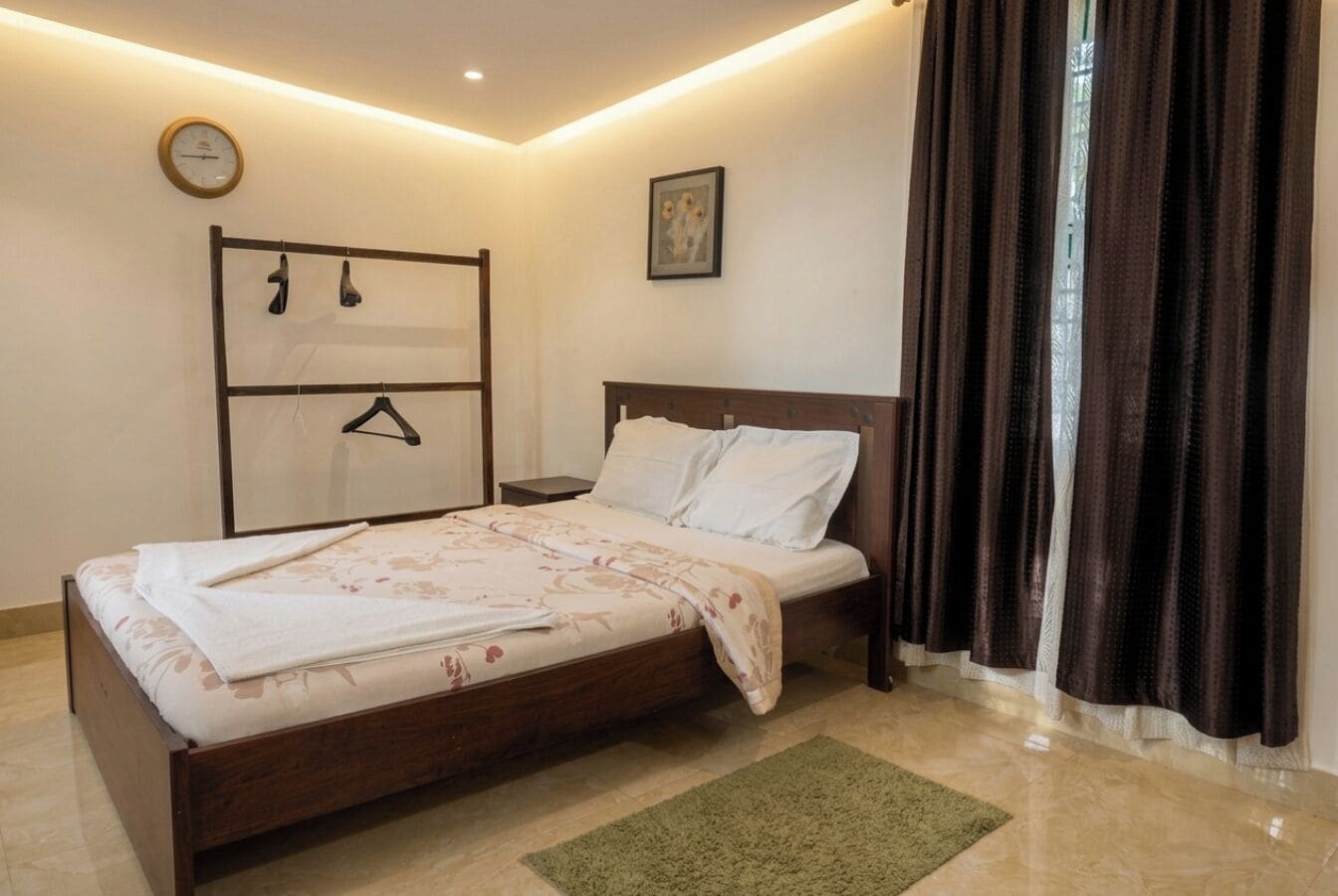 Un dormitorio con cama, mesita de noche, perchero en la pared, reloj y ventana con cortinas.
