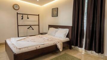 Un dormitorio con cama, mesita de noche, perchero en la pared, reloj y ventana con cortinas.