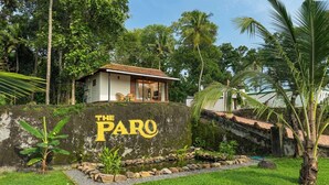 Una casa con un cartel que dice 'THE PARO' rodeada de abundante vegetación y un pequeño estanque.