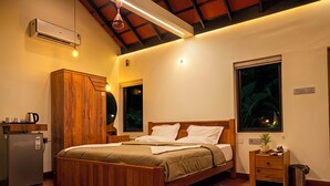 Un dormitorio con una cama de madera, una mesita de noche, una pequeña mesa, un aire acondicionado instalado en la pared y una ventana con vistas al cielo nocturno.