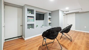 Quarto com piso de madeira, televisão fixada na parede e duas cadeiras pretas.