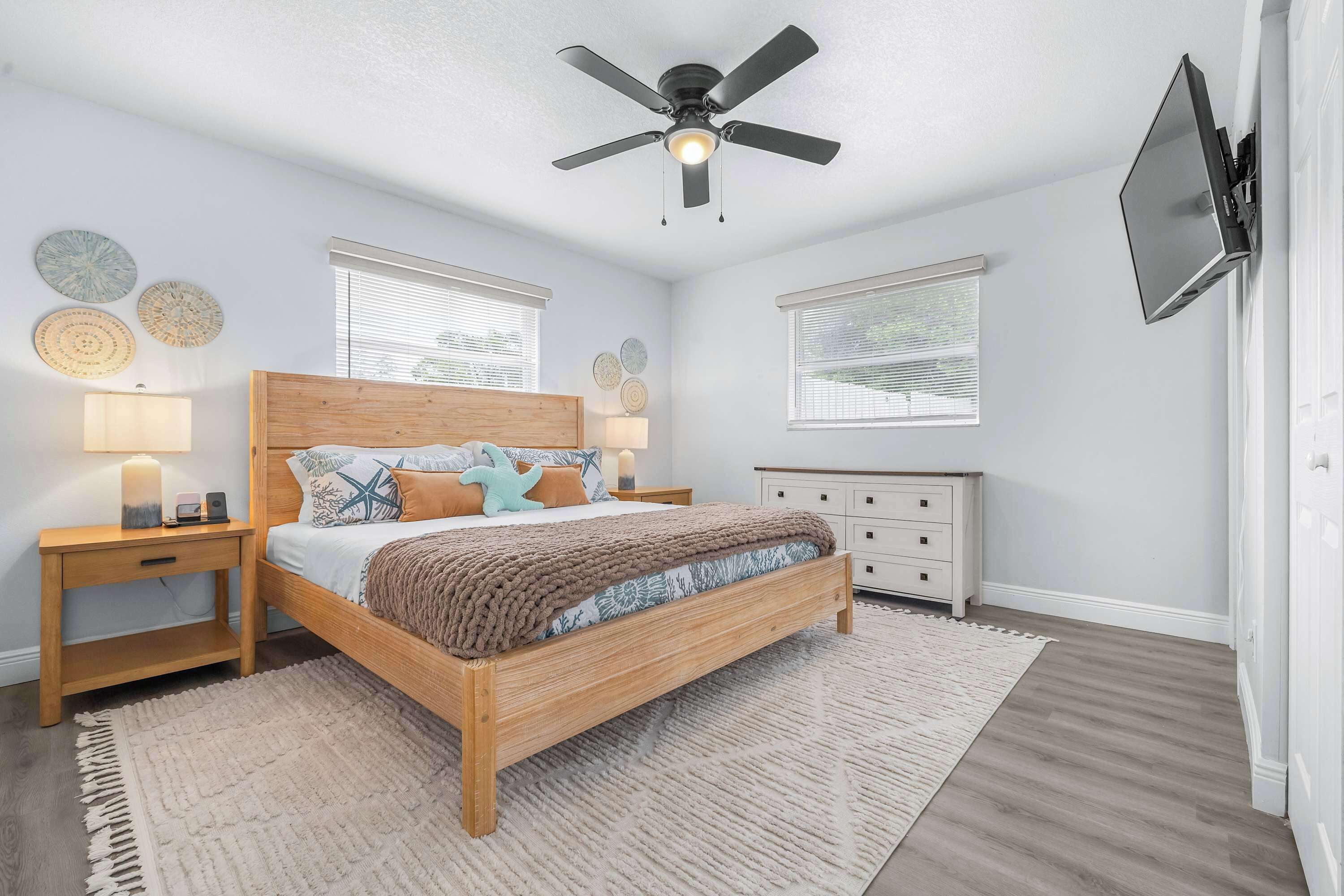 A bedroom with a wooden bed, nightstands, a ceiling fan, and a TV mounted on the wall.