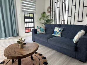A living room with a dark blue sofa, two patterned cushions, a round wooden coffee table, a woven rug, and a potted plant. - Lavi Zoli Stunning Private Villa in Grand Bay (Grand Baie)