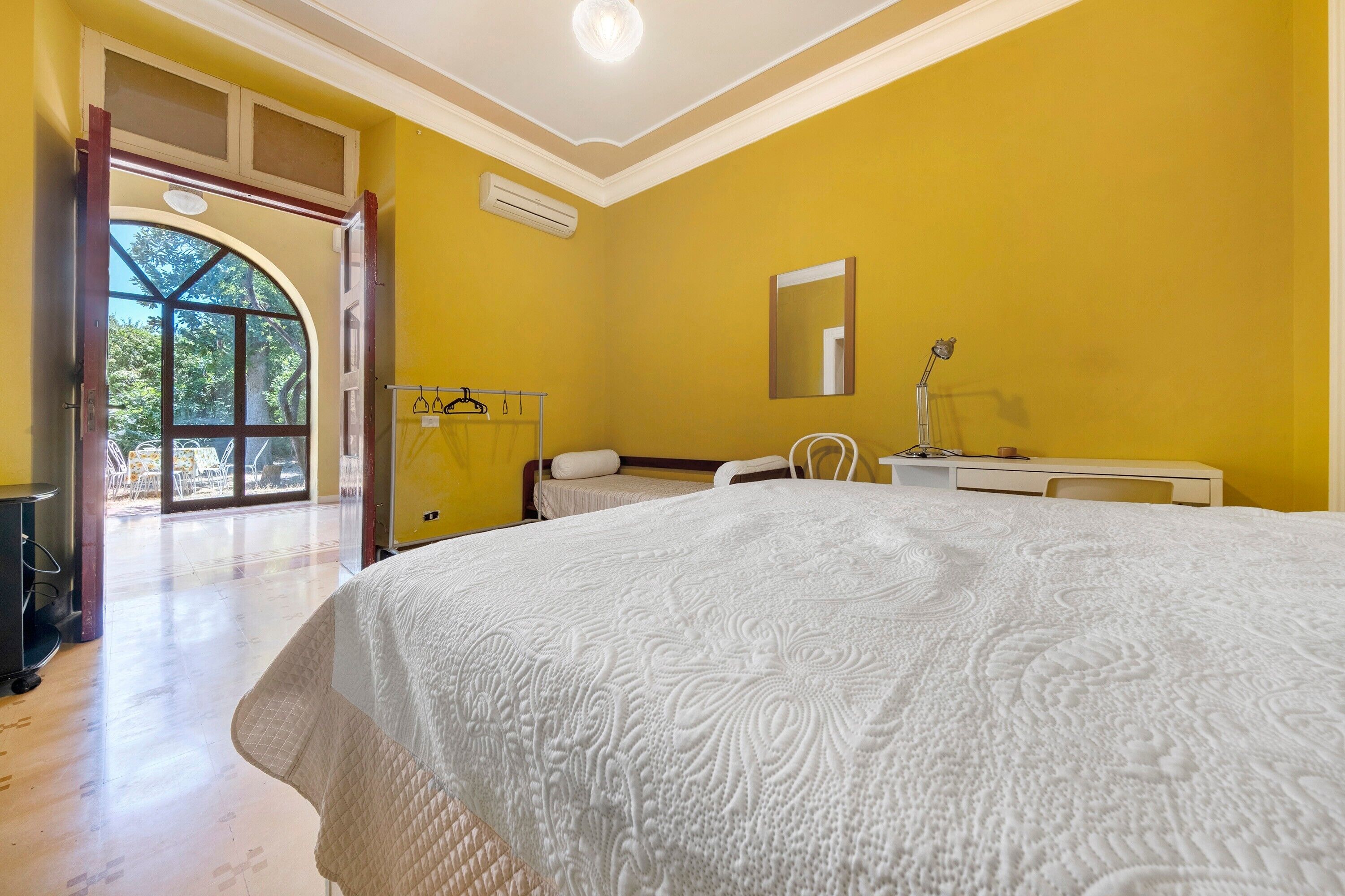 A bedroom with a large bed, a bedside table, a mirror, and a window.