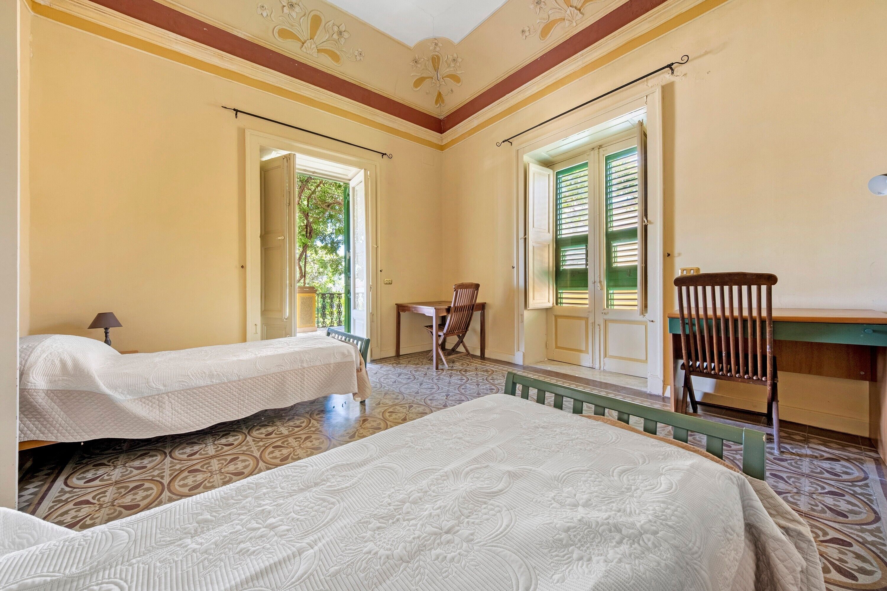 Una habitación con dos camas, una mesita, una silla y un ventanal con contraventanas.