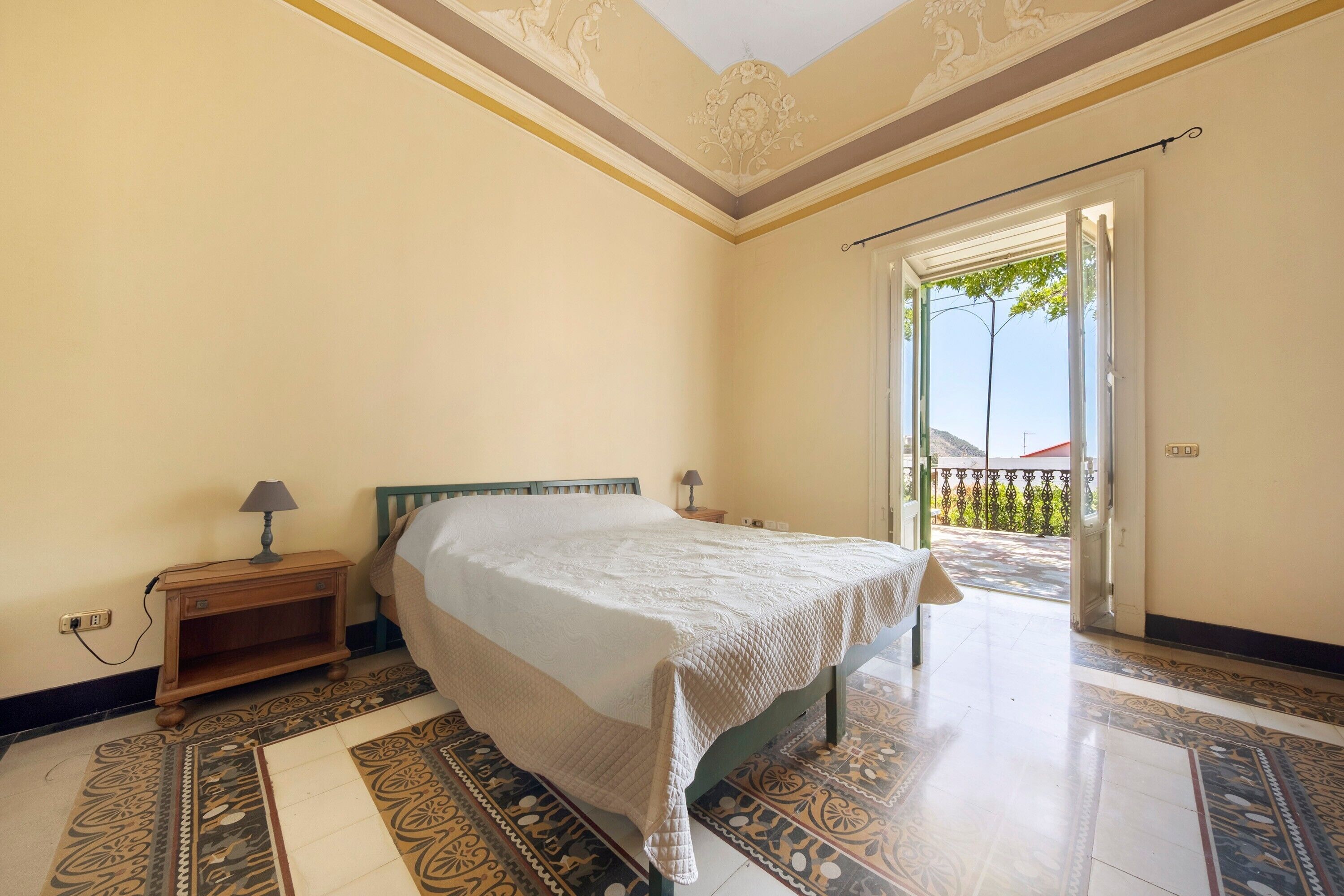 Une chambre à coucher avec un lit, une table de chevet, une lampe et une vue sur l’extérieur.