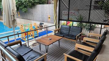 Un espacio de estar al aire libre techado con piscina, mobiliario de madera y una zona de juegos para niños.
