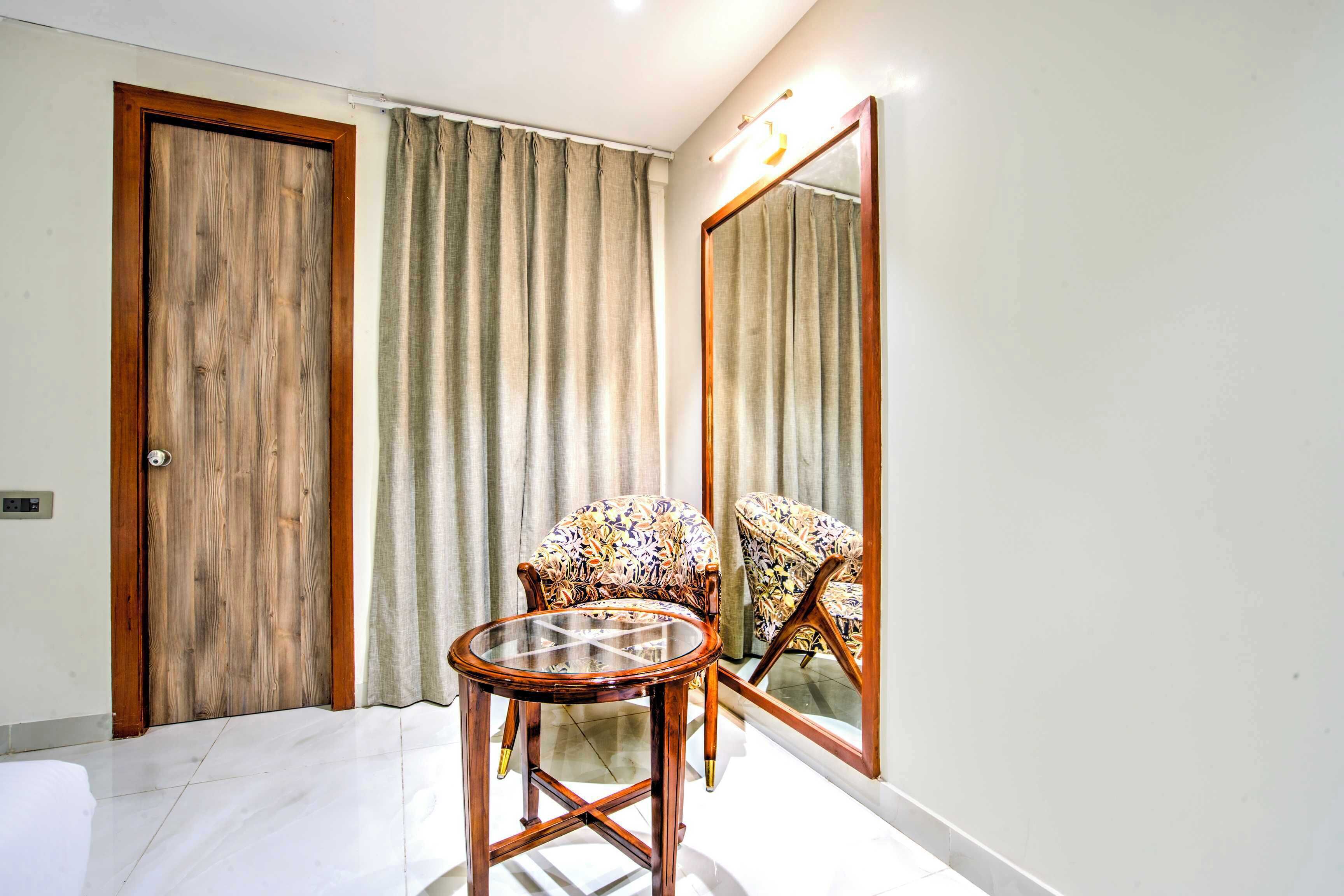 A room with a wooden door, a chair with a floral pattern, and a round glass table.