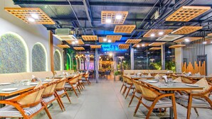 Un restaurante con mesas largas, sillas de mimbre, un diseño de techo moderno y paneles decorativos en las paredes.