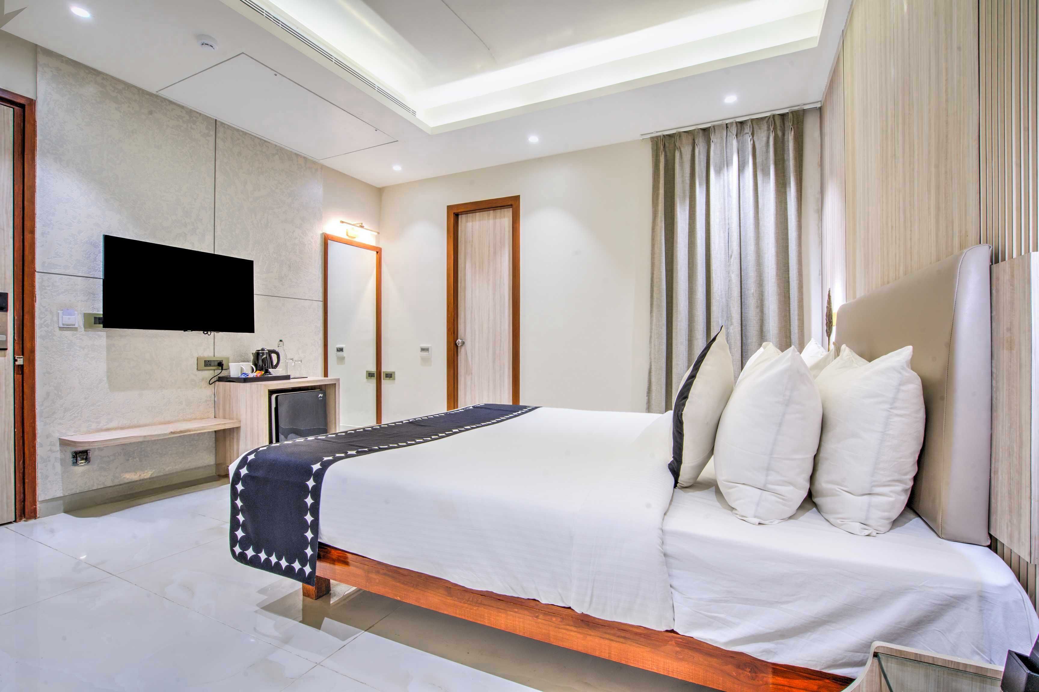 Una habitación de hotel moderna con una cama grande, un televisor de pantalla plana montado en la pared, una mesita de noche y una ventana con cortinas.
