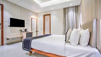 Una habitación de hotel moderna con una cama grande, un televisor de pantalla plana montado en la pared, una mesita de noche y una ventana con cortinas.