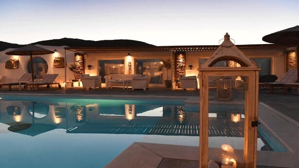 Un espace aménagé au bord de la piscine, avec des chaises longues, une lanterne en verre et un bâtiment à la façade en pierre.