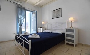 A bedroom with a bed, bedside tables, a nightstand, a lamp, a picture on the wall, and a window with curtains.
