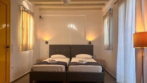 Une chambre avec deux lits, une porte en bois, un ventilateur de plafond et une lampe.