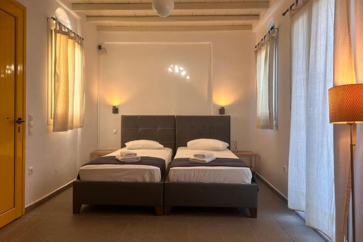 A room with two beds, a wooden door, a ceiling fan, and a lamp.