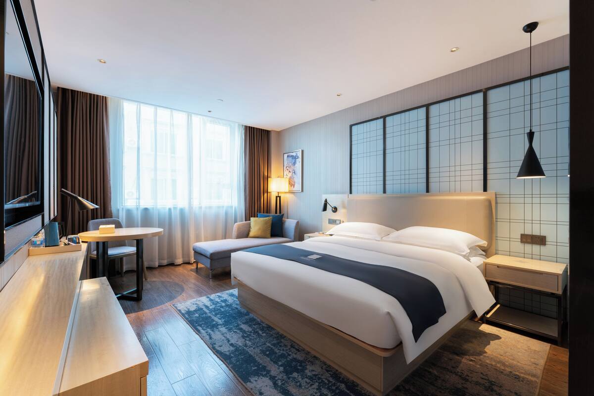 Ein modernes Hotelzimmer mit einem großen Bett, Nachttischen, einem Schreibtisch und Blick auf die Stadt.
