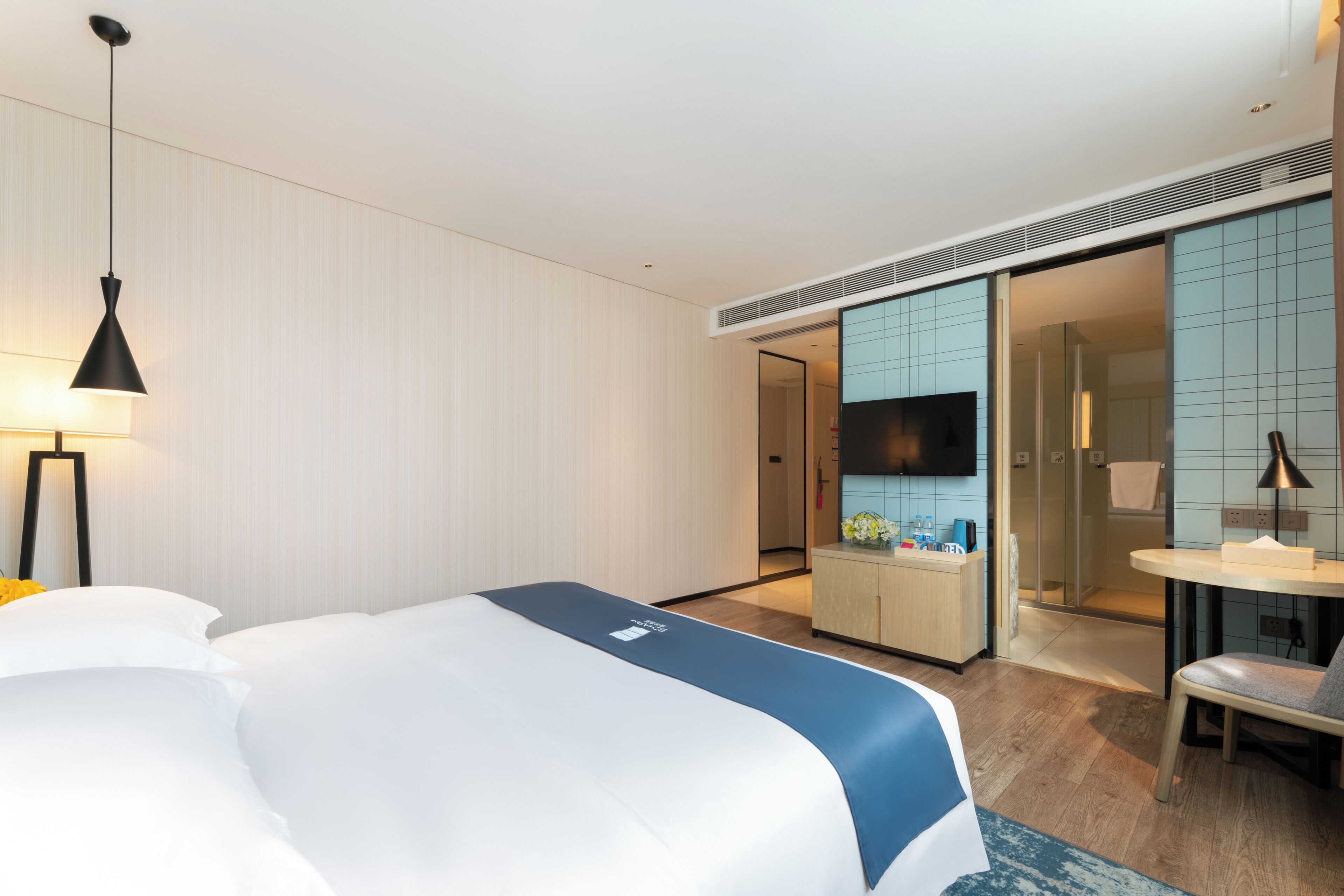 Ein modernes Hotelzimmer mit einem großen Bett, einem Schreibtisch mit Stuhl, einem Fernseher und einem durchgegangenen Tür erkennbaren Badezimmer.