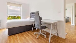 A bedroom with a bed, a desk, and a chair. There is a window with a view of greenery outside. - Cosy City Apartment in Manchester (Manchester)