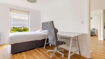 A bedroom with a bed, a desk, and a chair. There is a window with a view of greenery outside.