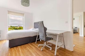 Ein Schlafzimmer mit Bett, Schreibtisch und Stuhl. Ein Fenster bietet Blick auf grüne Natur.