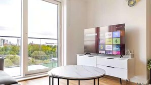 A modern living room with a large TV, a round table, and a view of a cityscape through a large window. - Cosy City Apartment in Manchester (Manchester)