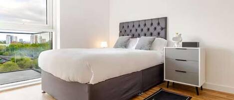 A modern bedroom with a large bed, a bedside table, and a view of a cityscape.