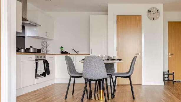 A modern kitchen with white cabinets, a wooden countertop, and a dining area with a round table and four chairs. - Cosy City Apartment in Manchester (Manchester)