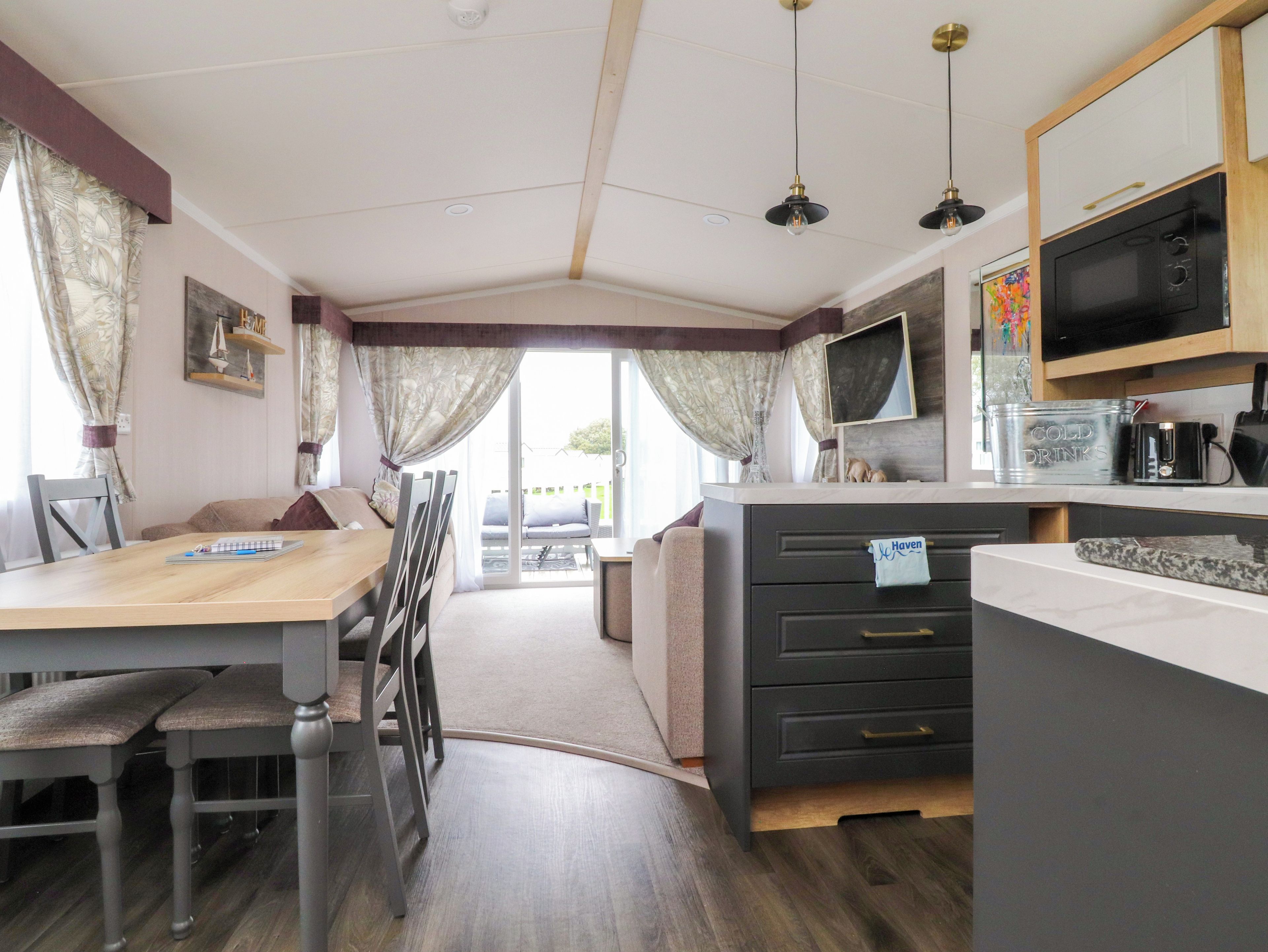 Una habitación acogedora con una mesa de comedor, sillas, un sofá, una zona de cocina con microondas y un televisor.