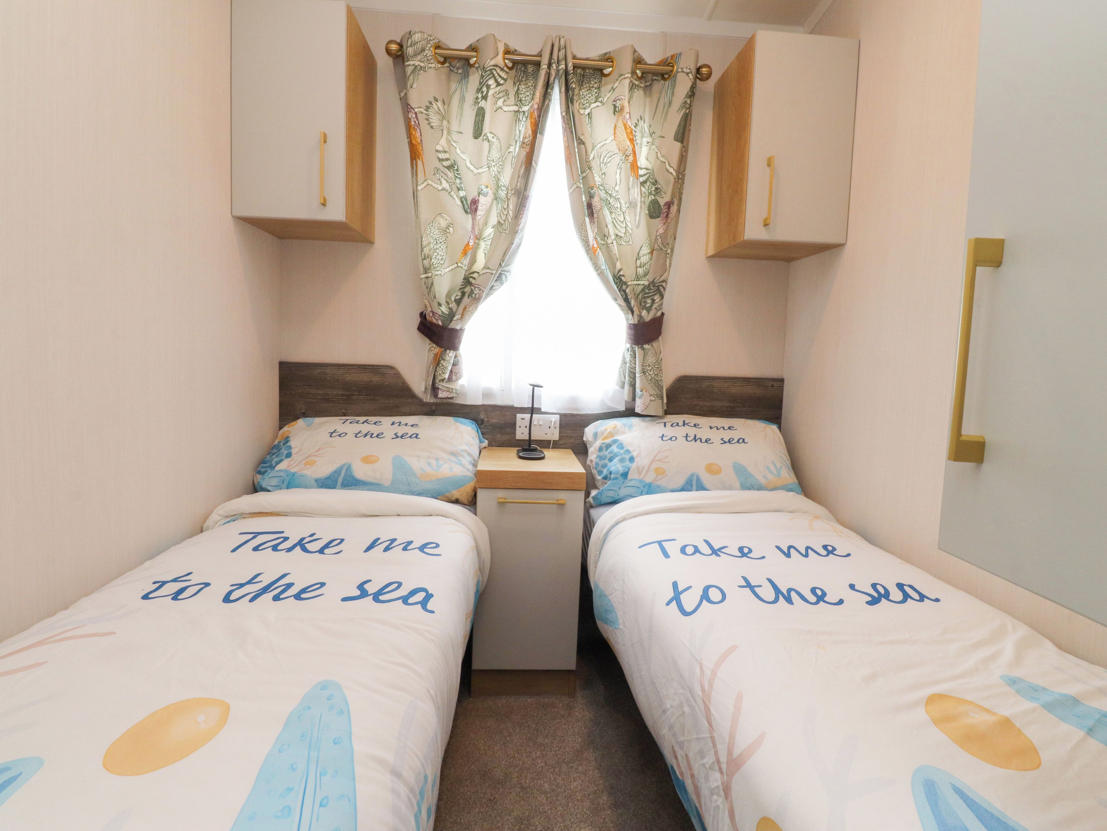 A bedroom with two beds, each with a pillow featuring the phrase 'Take me to the sea.'