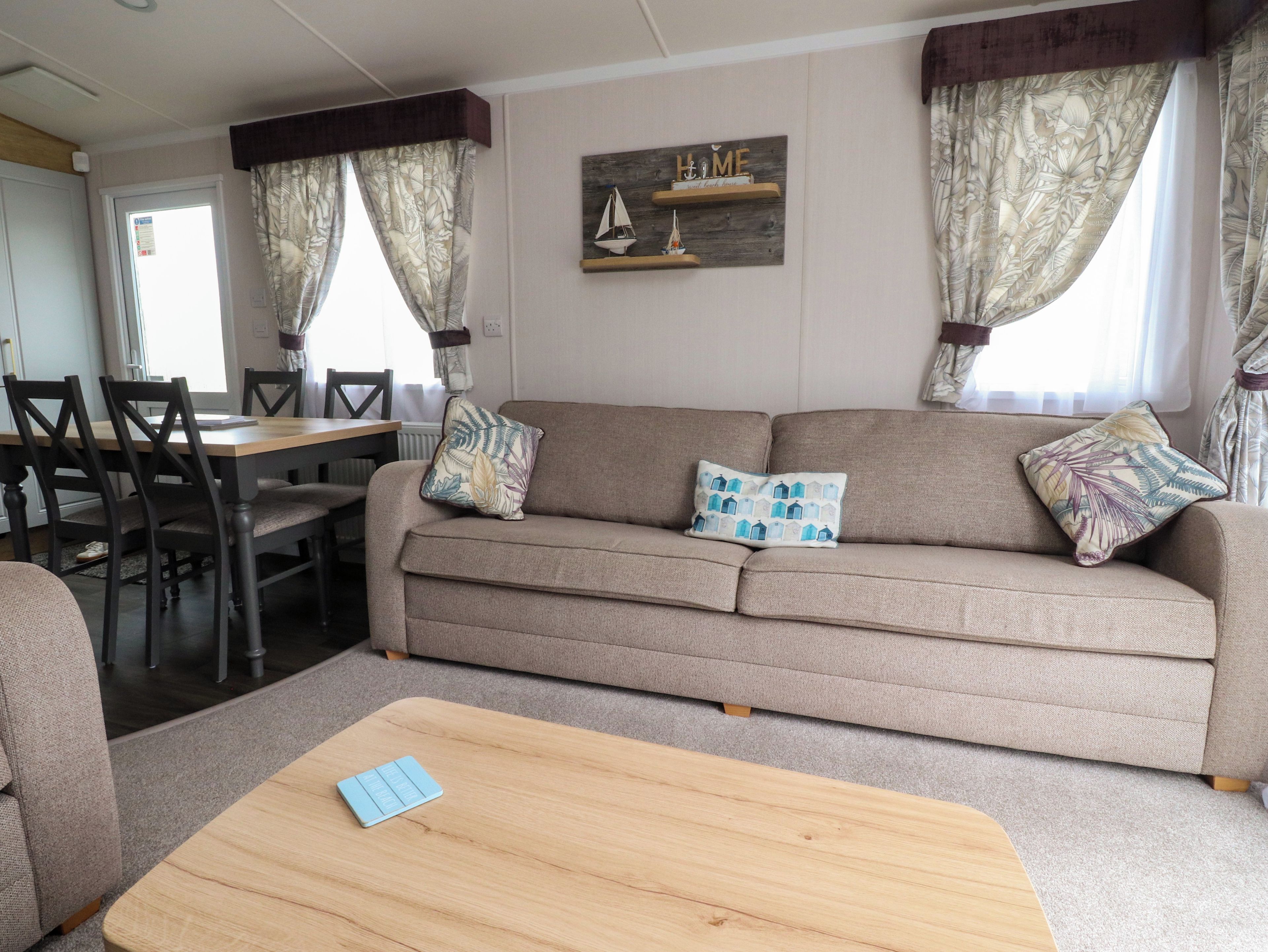 A living room with a sofa, two pillows, a wooden coffee table, a dining table with chairs, and a window with curtains.