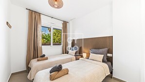 Hotellihuone, jossa on kaksi sänkyä, ikkuna, jossa on verhot, puinen sängynpääty ja riippuvalaisin.