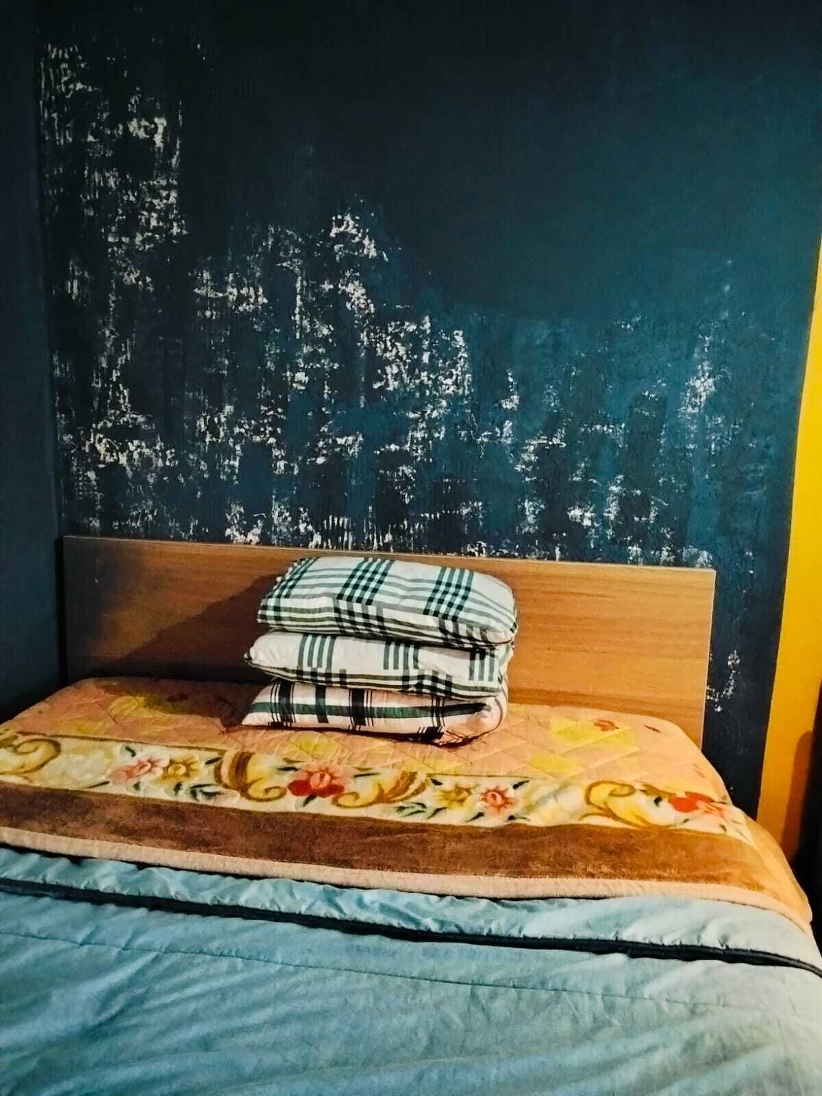 En seng med et blomstret sengetæppe, et træhovedgærde og en mørk væg med afskallende maling.