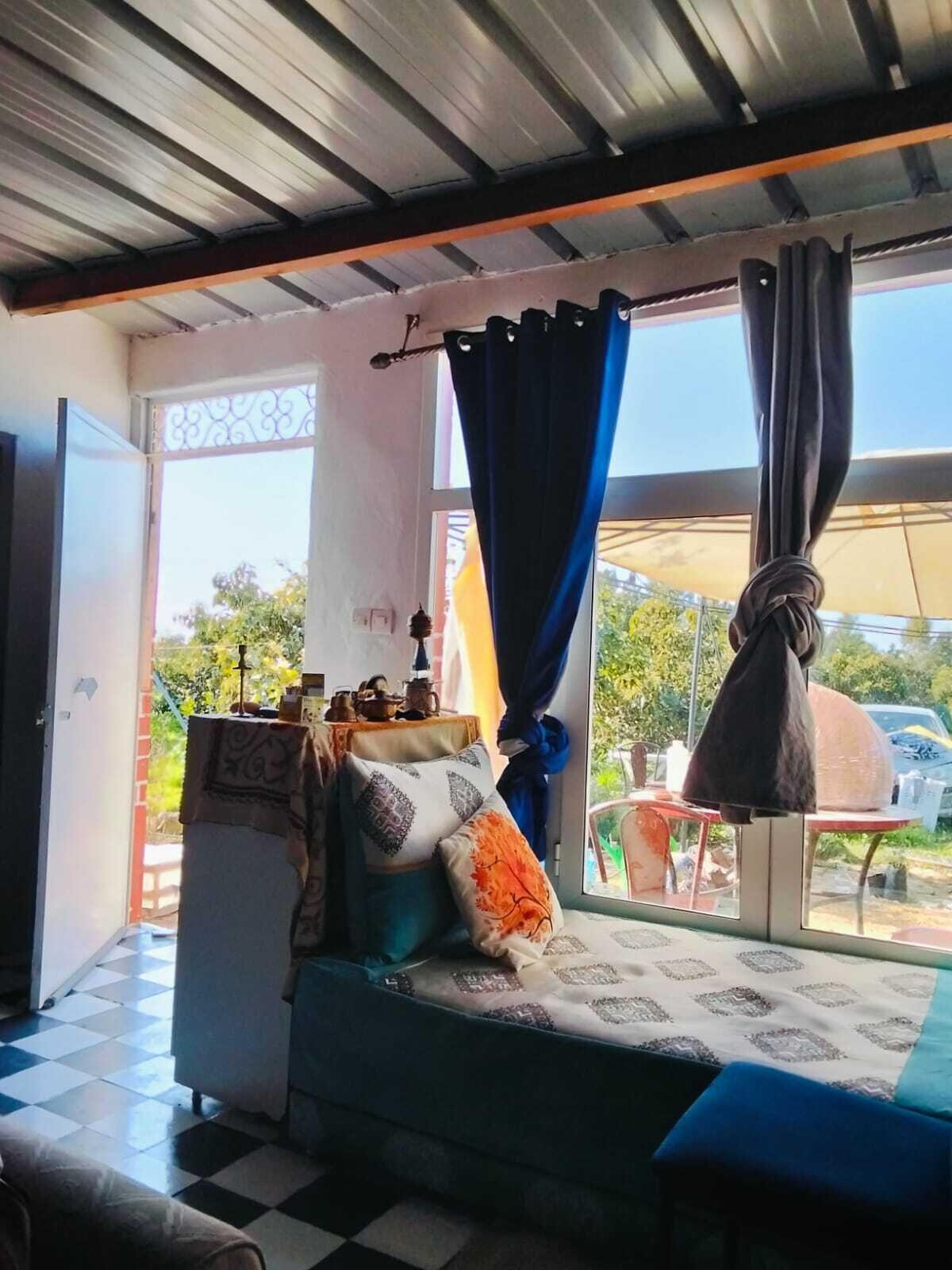 A room with a bed, a table with a lamp, and a view of the outdoors.