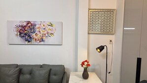 Un saló modern amb un sofà gris, una taula blanca petita amb un vas de flors, una làmpada de peu i una obra d'art emmarcada a la paret.
